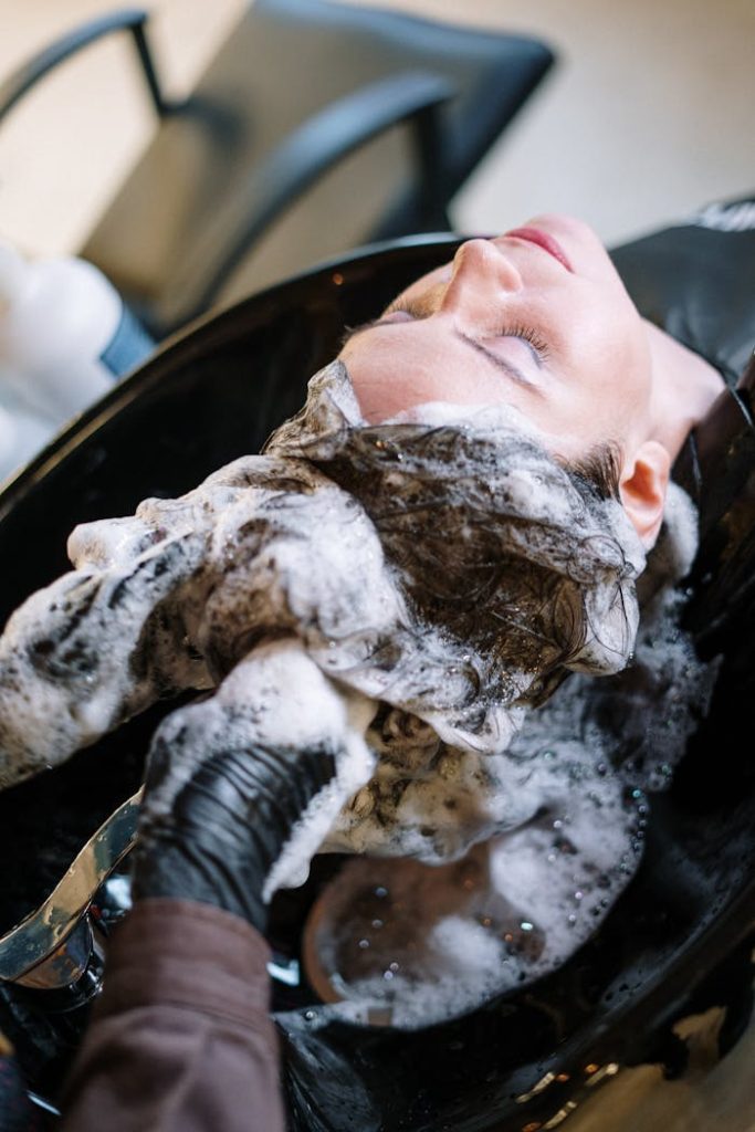 pexels photo 3993444 A woman getting her hair washed at a salon sink by a professional stylist wearing black gloves.
