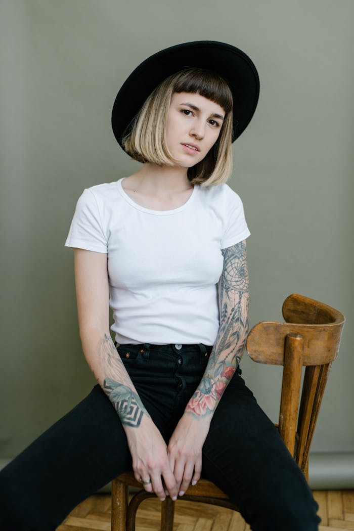 projects-header Young confident female in hat and denim jeans with tattoos relaxing on chair and looking at camera in studio